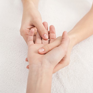 Refleksologia dłoni - zbliżenie na wewnętrzną lewą dłoń kobiety której środkowy palec jest masowany przez terapeutkę