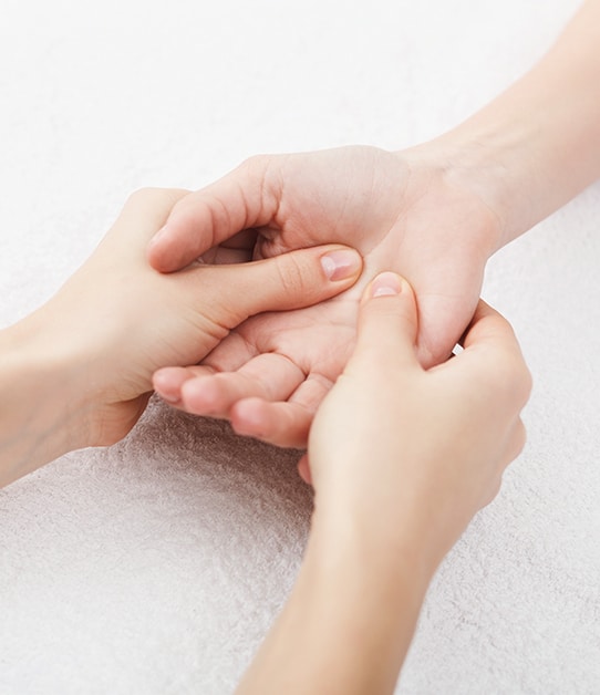 Refleksologia dłoni - zbliżenie na wewnętrzną prawą dłoń kobiety której śródręcze jest masowane przez terapeutkę